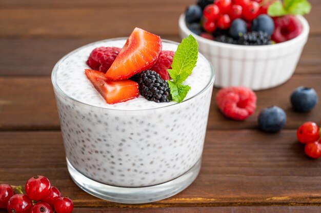 Budino di chia alla vaniglia con frutti di bosco freschi e miele in un bicchiere su uno sfondo di legno scuro