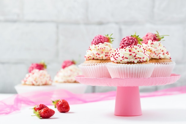 Vanilla cupcakes decorated with strawberries on a pink cake stand