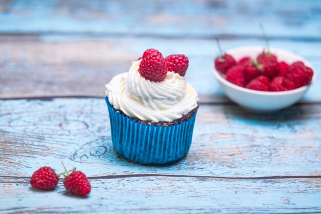 Vanilla cupcakes with cream and raspberries on a blue wooden background Birthday muffins for party