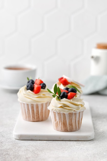 Vanilla cupcakes with fresh berries buttercream green leaves on grey background  Dessert Copy space