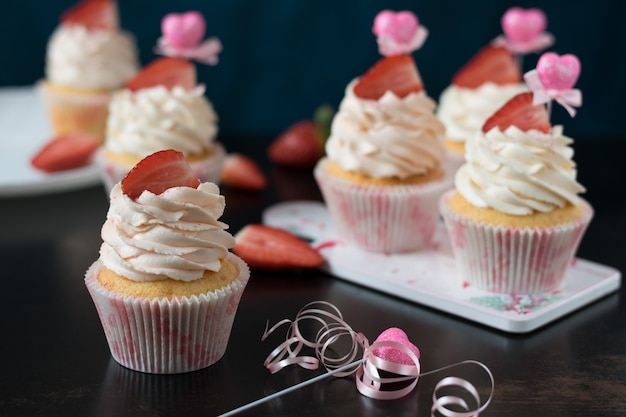 Vanilla cupcakes with fresh strawberries on a dark surface