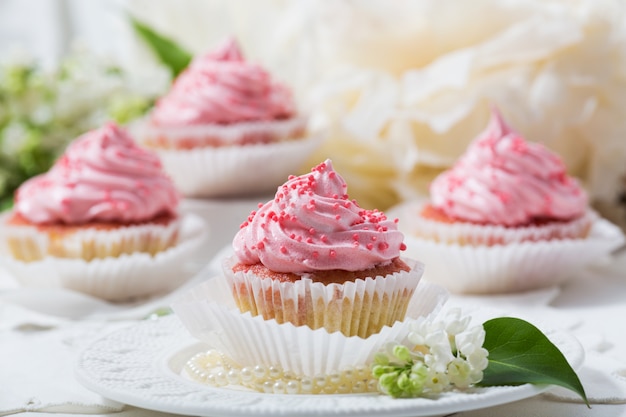 Cupcakes alla vaniglia con crema rosa su un tavolo bianco, fiore bianco e foglia