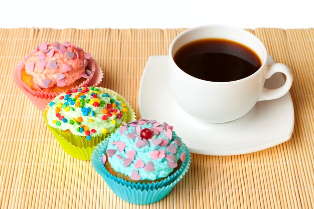 Vanilla cupcakes with whipped cream and colored sprinkles with a cup of coffee.