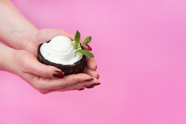 Vanilla ice cream ball in fresh coconut half decorated with mint leaves on a pink background
