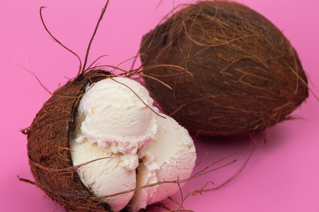 Vanilla ice cream balls in an empty coconut decorated with mint leaves on a pink background
