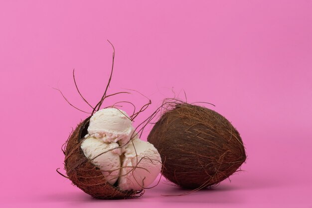 Vanilla ice cream balls in an empty coconut decorated with mint leaves on a pink background.