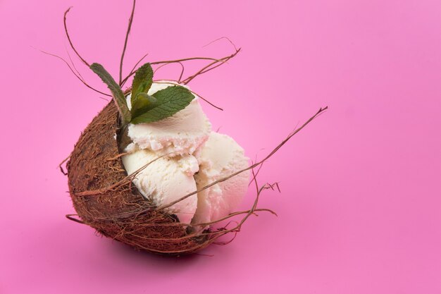 Vanilla ice cream balls in an empty coconut decorated with mint leaves on a pink background.