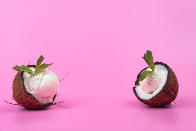 Vanilla ice cream balls in fresh coconut halves decorated with mint leaves on a pink background