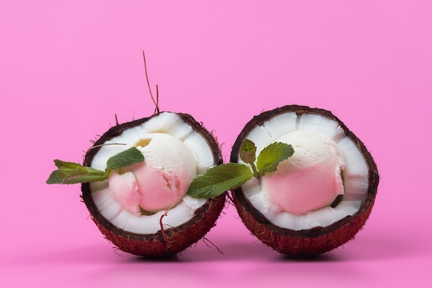 Vanilla ice cream balls in fresh coconut halves decorated with mint leaves on a pink background