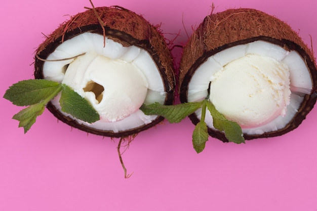 Vanilla ice cream balls in fresh coconut halves decorated with mint leaves on a pink background