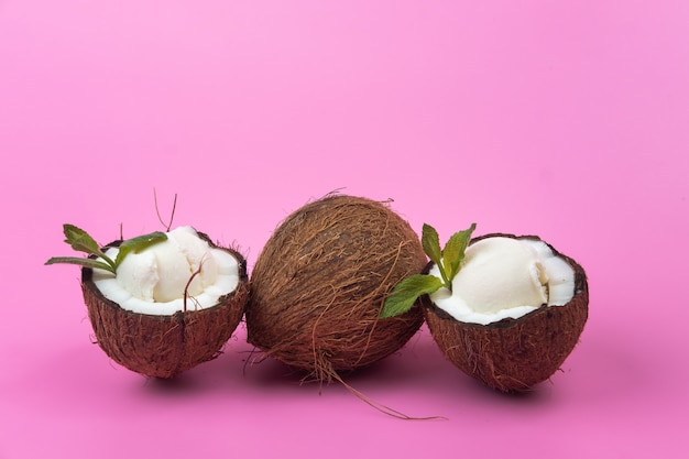 분홍색 배경에 민트 잎으로 장식 된 신선한 코코넛 반쪽에 바닐라 아이스크림 볼