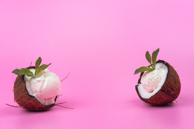 핑크 바탕에 민트 잎으로 장식 된 신선한 코코넛 반쪽에 바닐라 아이스크림 볼.