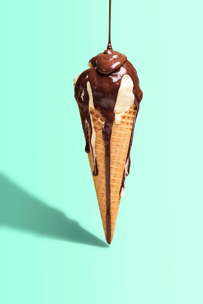 Photo vanilla ice cream cone with melted chocolate topping on green background harsh light summer dessert