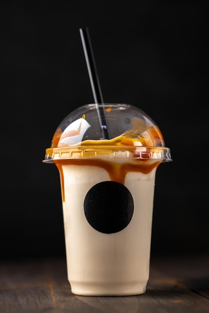 어두운 배경에 있는 플라스틱 유리에 바닐라 우유 칵테일 테이크아웃 플라스틱 컵에 든 카라멜 밀크셰이크