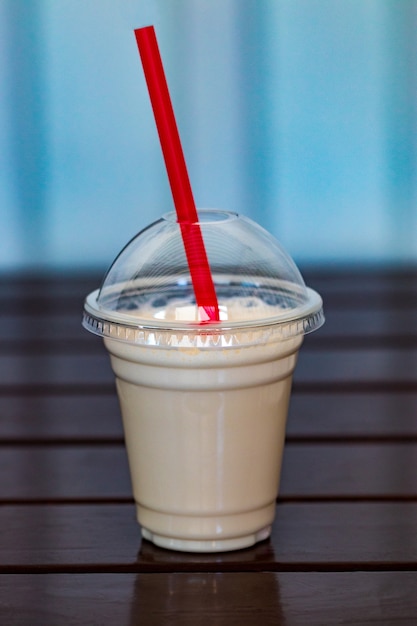 Photo vanilla milkshake covered with whipped cream in plastic glass on wooden background.