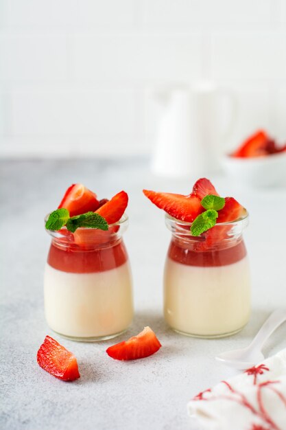 Panna cotta alla vaniglia e fragole fresche, foglie di menta sulla superficie del tavolo in cemento grigio.