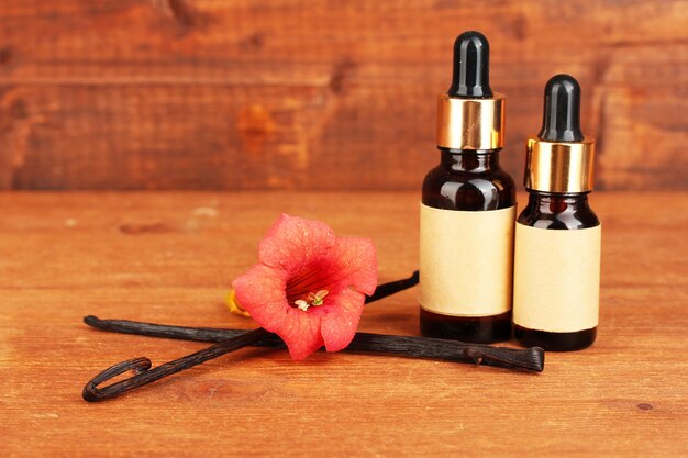 Vanilla pods with essential oil on wooden background closeup