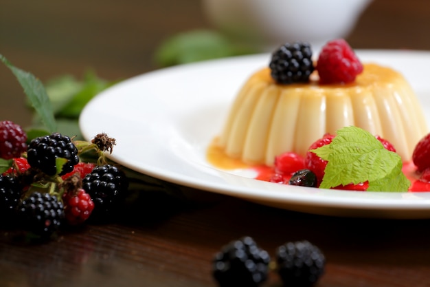 Vanilla pudding with berries and cream on a white plate close-up