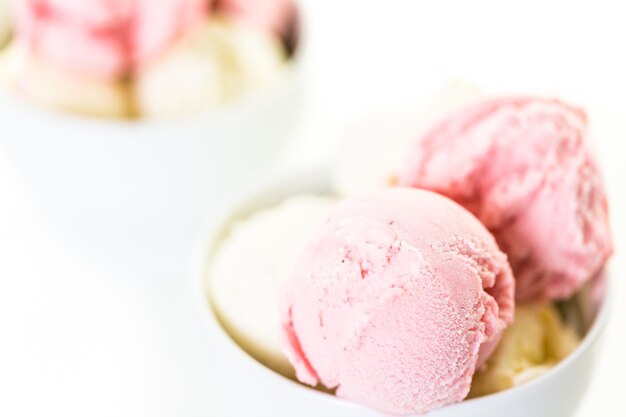 Vanilla and strawberry ice cream scoops in a white cup.