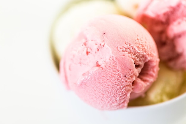 Vanilla and strawberry ice cream scoops in a white cup.