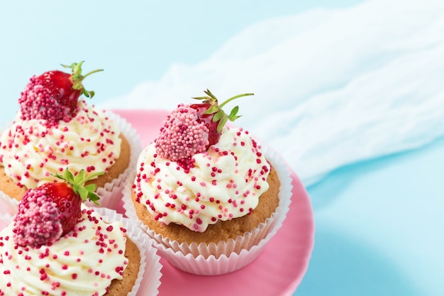 Vanille cupcakes versierde aardbeien op een roze taartstandaard met blauwe achtergrond