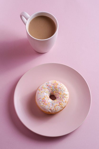 Vanille donut met hagelslag op plaat in de buurt van kopje koffie, zoete geglazuurde dessert eten en warme dranken op roze minimale achtergrond, hoekmening