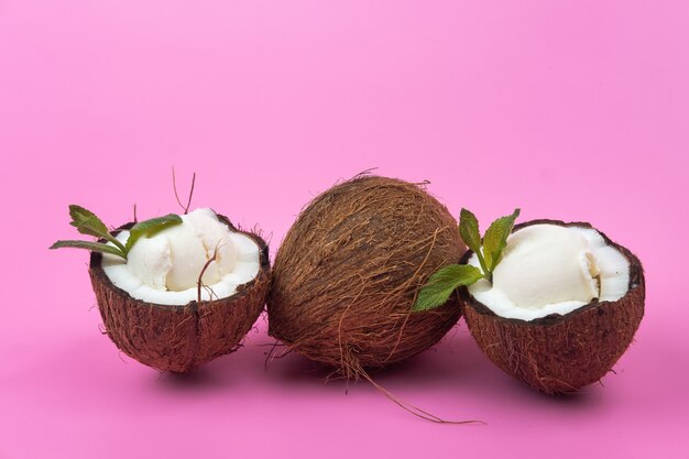 Vanille-ijsballetjes in verse kokosnoothelften versierd met muntblaadjes op een roze achtergrond