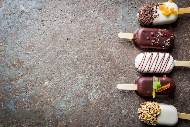 Vanille ijslollys met chocolade vacht en top met amandelnoten en snoepjes, bovenaanzicht.