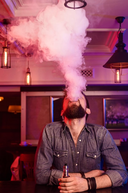 Vape。蒸気の雲の中で男を吸う。写真はアークバーで撮影されています。アークショップ