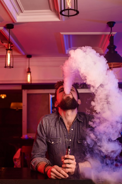 Vape。蒸気の雲の中で男を吸う。写真はアークバーで撮影されています。アークショップ