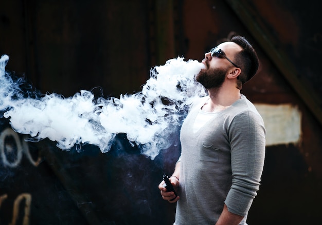 Photo vaper with beard in sunglasses vaping outdoor