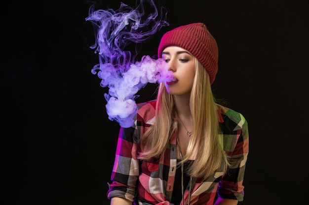 Vaping girl. Young hipster woman vape e-cig on studio on black background. Hip-hop style. Close up.