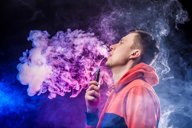 Vaping man holding a mod. A cloud of vapor. dark blue background.