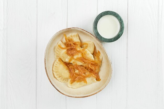 Vareniki met aardappel en zure room in een bord op een witte houten dumplings als achtergrond