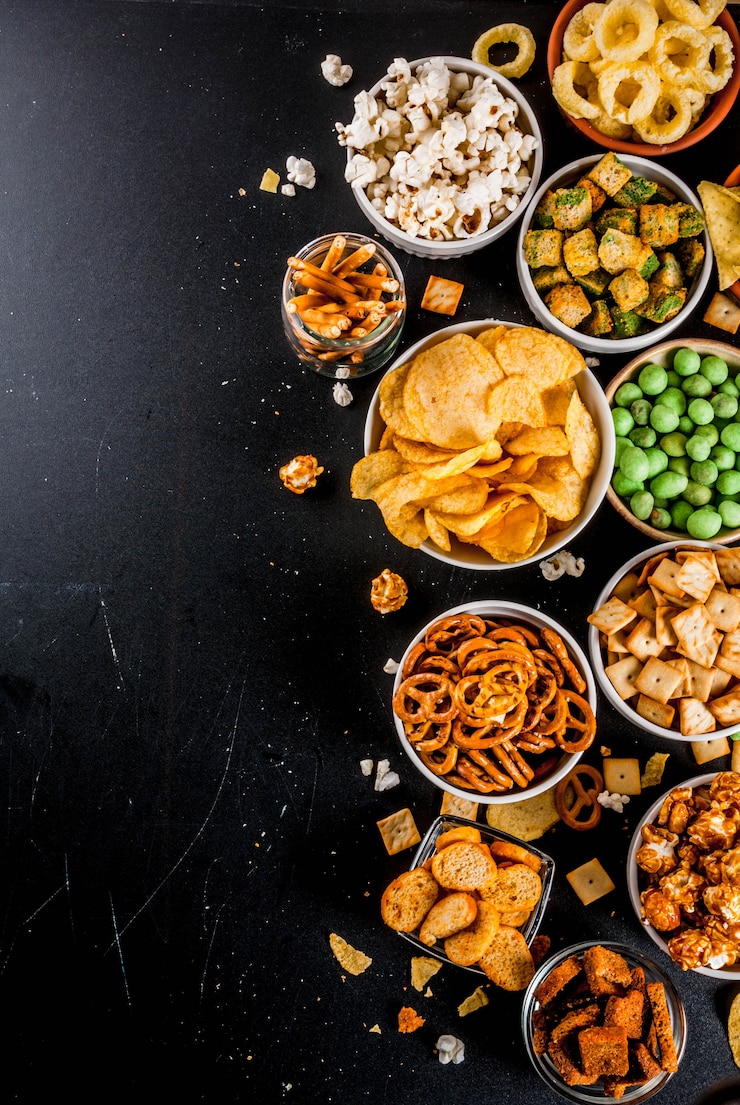 Foto variatie verschillende ongezonde snacks crackers, zoete gezouten popcorn, tortilla's, noten, rietjes, bretsels