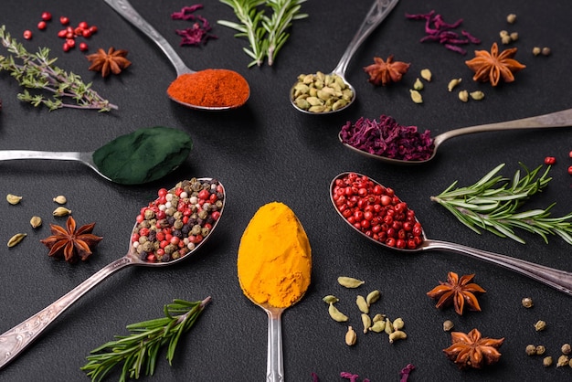 Variation of spices in metal spoons paprika turmeric cardamom a mixture of allspice thyme rosemary and salt on a dark concrete background