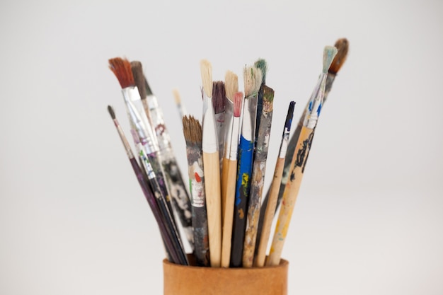 Varieties of paint brushes in jar against white background