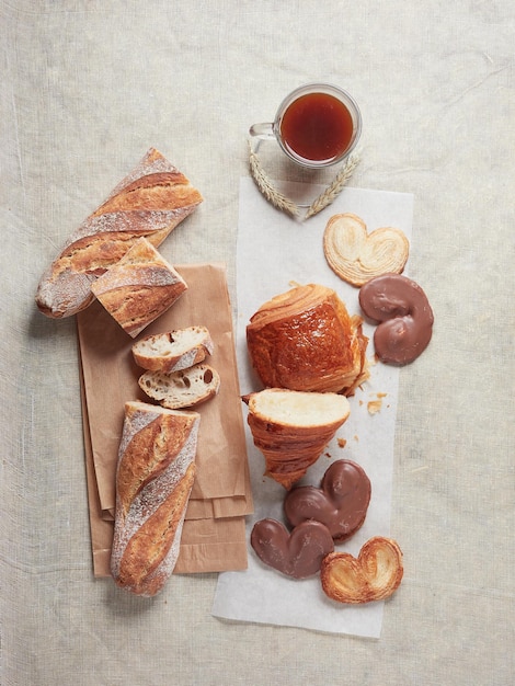 Variety of breakfast bakery products palmiers croissants and napolitains with loaf of bread and cup of coffee Top view