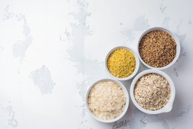 Varietà di fiocchi di cereali riso, miglio, grano saraceno, farina d'avena. superfood in ciotole di ceramica bianca di legno