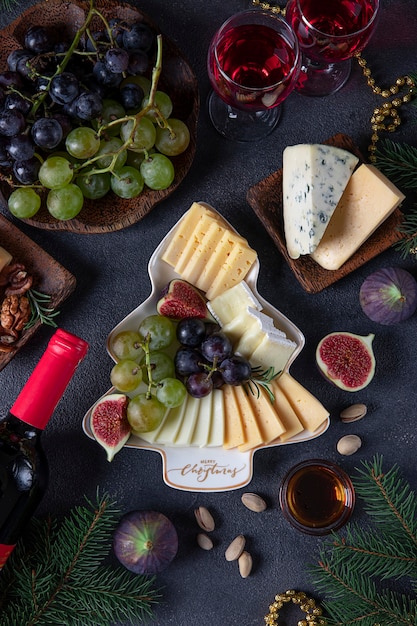 Variety of cheese and fruits served in plate as Christmas tree, on dark gray background with two glasses of wine. New Year's Eve Party Snack