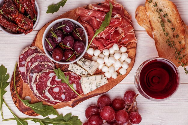 Variety of cheese and meat, olives, grapes, arugula on white table