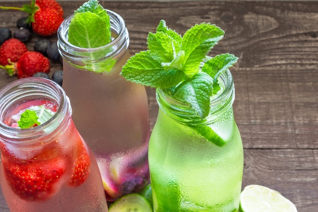 Foto varietà di bevande fredde estive in piccole bottiglie con frutta, bacche, cetrioli e menta