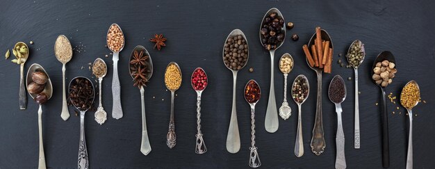 Variety of colorful spices in spoons on black stone background top view banner