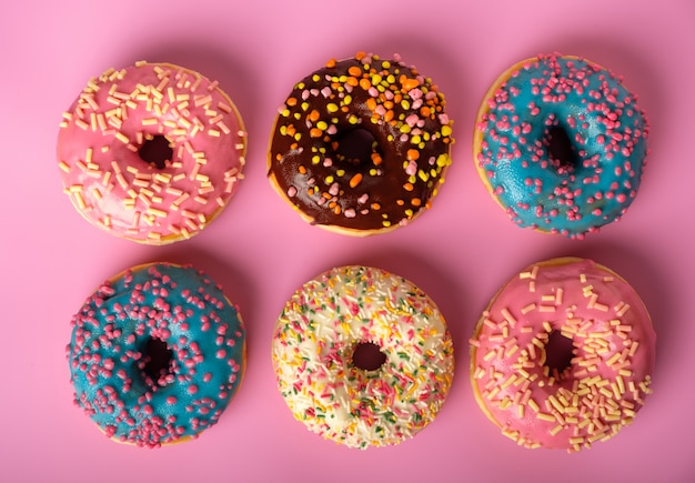 Variety of colorful tasty glazed donuts on a colored