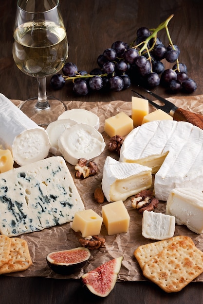 Variety of different cheese with wine, fruits and nuts. Camembert, goat cheese, roquefort, gorgonzolla, gauda, parmesan, emental