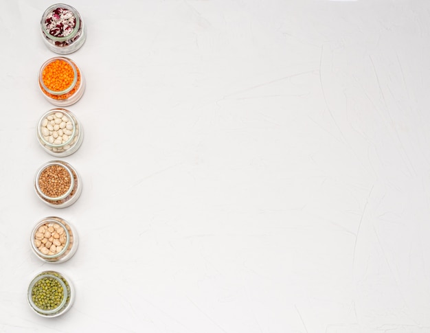 유리 항아리에 채식주의자를위한 다양한 건조 시리얼 : 렌즈 콩, 병아리 콩, 콩, 흰색 표면에 메밀