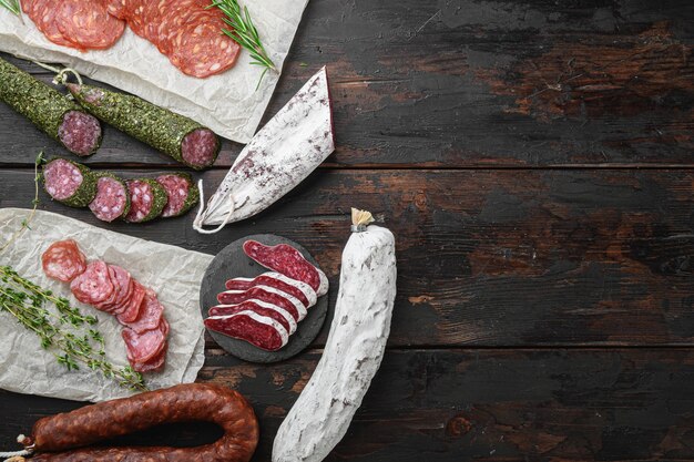 Variety of dry cured  chorizo, fuet and other sausages cut in slices with herbs on old wooden table, flat lay with copy space.