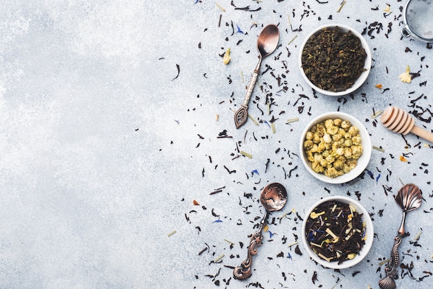 Variety of dry tea leaves and flowers in bowl on grey background.