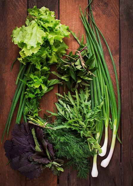 Foto erbe organiche fresche di varietà (lattuga, rucola, aneto, menta, lattuga rossa e cipolla) sulla tavola di legno in stile rustico. vista dall'alto