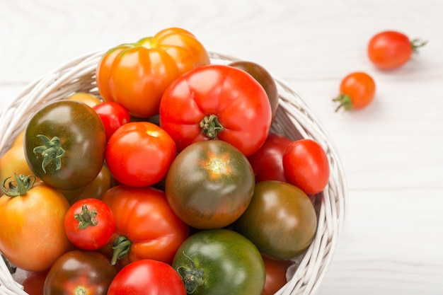 Variety Fresh tomatoes in basket on wooden . top view